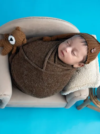 This little gentleman is sleeping so soundly on a miniature sofa. The brown knit wrap and tiny teddy bear add to the cozy and adorable scene.