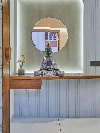 The entrance foyer features a serene Buddha statue on a floating wooden shelf, set against a fluted panel and backlit for a calming effect.
