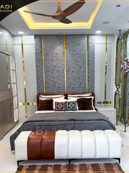 A master bedroom that defines modern luxury with its striking grey and gold theme. The design includes a floor-to-ceiling upholstered headboard with gold inlay, a custom two-tone bench, and elegant metallic room dividers for a touch of glamour.