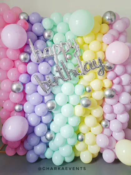 A full wall of pastel rainbow balloons with a silver 'Happy Birthday' foil balloon, creating a stunning photo backdrop.