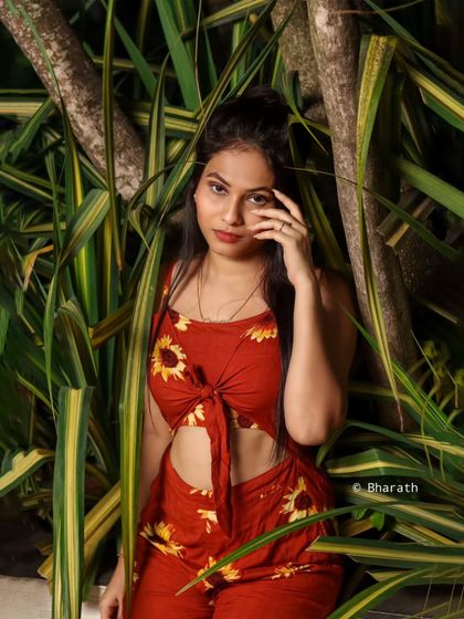 A vibrant outdoor shot of a model in a red, sunflower-print two-piece outfit. The lush green background makes the red color pop.