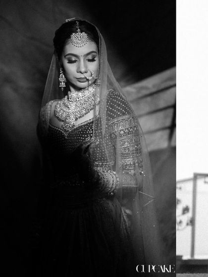 A dramatic black and white portrait of the bride, emphasizing the intricate details of her jewelry and the delicate texture of her veil.