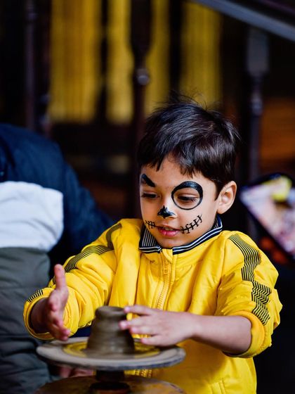 Here, a young guest with fun face paint gets hands-on with our pottery wheel activity. I provide a space for children to explore their creativity during our Sunday brunches, making it a fun and educational experience.