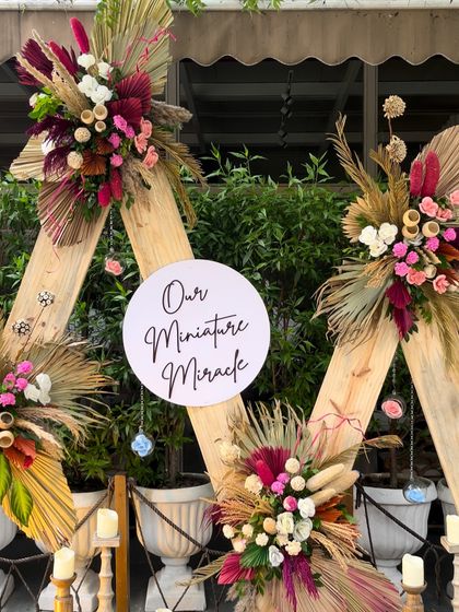 "Our Miniature Miracle." This close up shows the intricate floral work on the boho-themed baby shower backdrop. We used a mix of dried palms, pampas grass, and colorful flowers to create a rich, textured look.