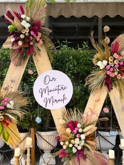 "Our Miniature Miracle." This close up shows the intricate floral work on the boho-themed baby shower backdrop. We used a mix of dried palms, pampas grass, and colorful flowers to create a rich, textured look.