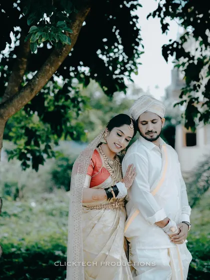 A tender and candid moment between a bride and groom in their traditional South Indian wedding attire, captured outdoors in a quiet, natural setting.