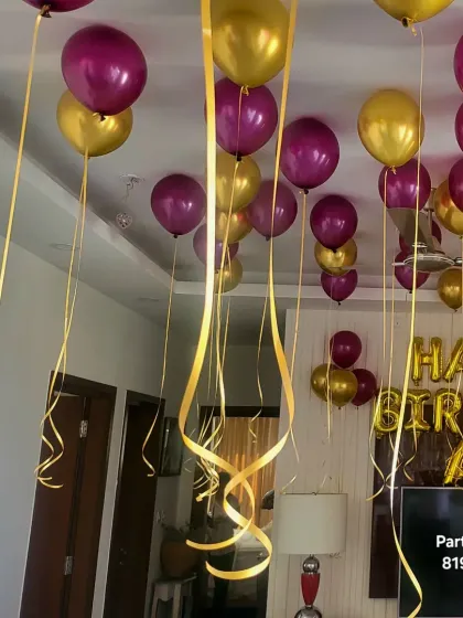 Purple and gold helium balloons with long, curly ribbons covering the ceiling for a birthday surprise.