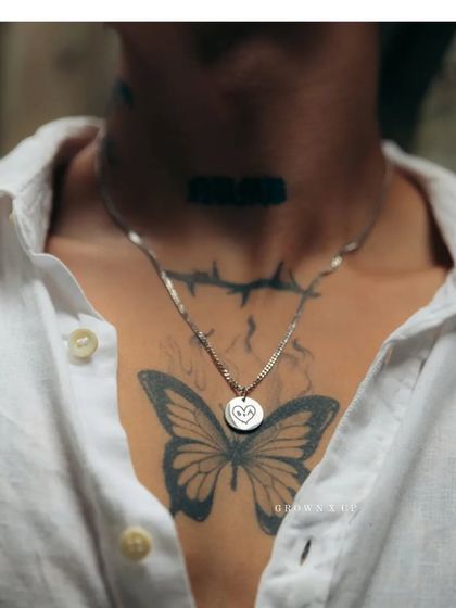 A silver-toned round pendant engraved with a simple, hand-drawn style heart. This piece, worn against a butterfly tattoo, shows how my jewelry can complement your personal story and style.