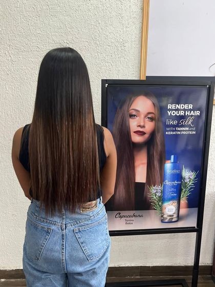 A client posing next to a poster for a keratin protein treatment, showing off her own silky, straight hair.