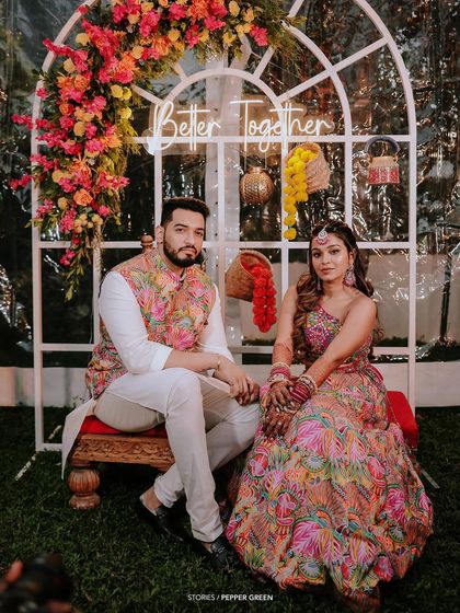 Arya and her groom seated before their ceremony, framed by a beautiful floral arch. This shot captures the calm before the celebration begins, highlighting the stunning decor and traditional attire.