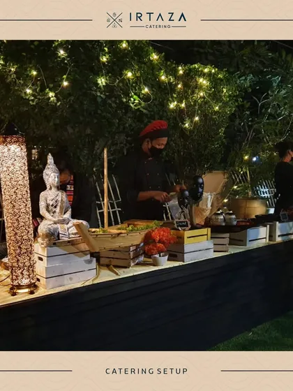 A beautiful outdoor evening setup with rustic wooden crates and string lights. The serene Buddha statue adds a touch of tranquility to this live station, perfect for a relaxed garden party.