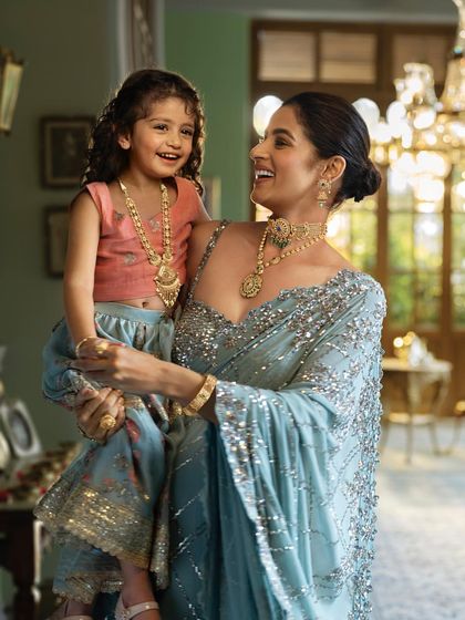 A heartwarming mother-daughter moment from the Tanishq 'Dharohar' campaign. The styling uses complementary pastel outfits and coordinated gold jewellery to visually represent the bond and shared heritage between generations.