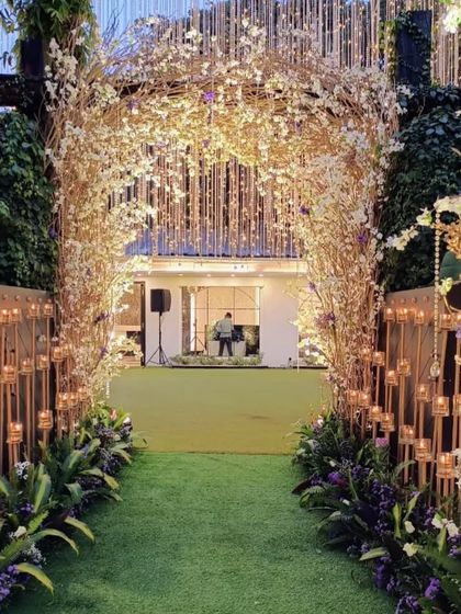 This enchanting entranceway uses an arch of rustic branches and white blossoms, lined with candles. The path leads into a lush green lawn, creating a beautiful transition from the entrance to the main event area.