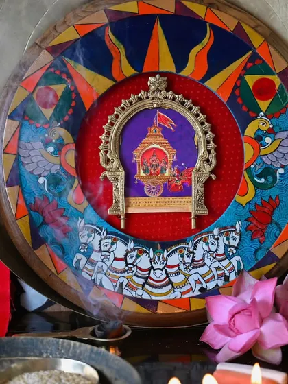 A beautifully staged shot of the Surya frame, surrounded by offerings of lotus flowers and diyas. The artwork depicts Surya's chariot drawn by seven horses, symbolizing the seven meters of the Vedas, all hand-painted on the restored frame.