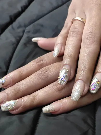 A dazzling set of long, square-tipped extensions with a glitter base, enhanced with large iridescent crystals and smaller gold studs.