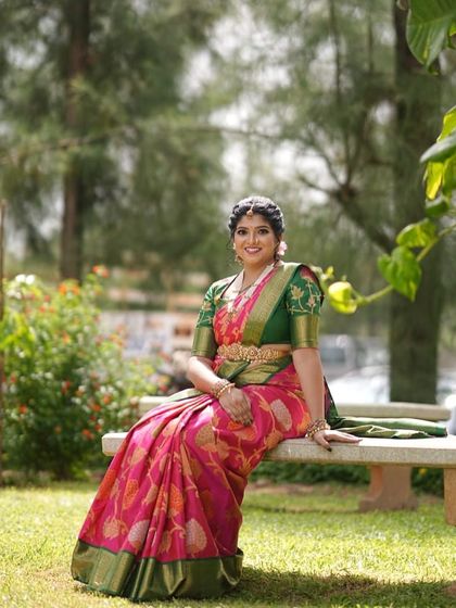 Seated in a garden, Devika's pink saree looks vibrant and beautiful against the natural greenery.
