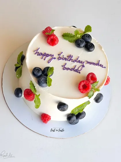 A simple yet beautiful celebration cake with chocolate buttercream, decorated with fresh raspberries, blueberries, and mint leaves for a pop of color and flavor.