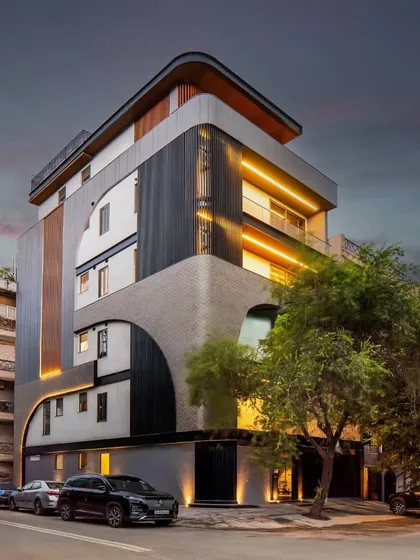 This builder floor in Patel Nagar, Delhi, demonstrates how modern geometry can redefine an urban streetscape. The facade's composition of symmetrical curves, aluminum louvers, and textured mortar creates a balanced and restrained look, especially when highlighted by evening lights.