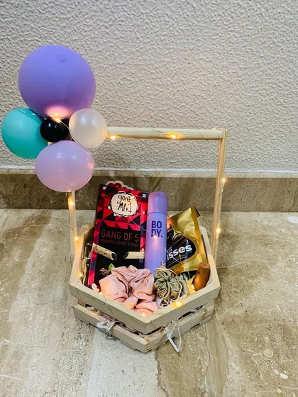 A simple yet sweet gift basket featuring a body spray, chocolates, and other small treats. The mini balloons add a festive and celebratory touch to the arrangement.