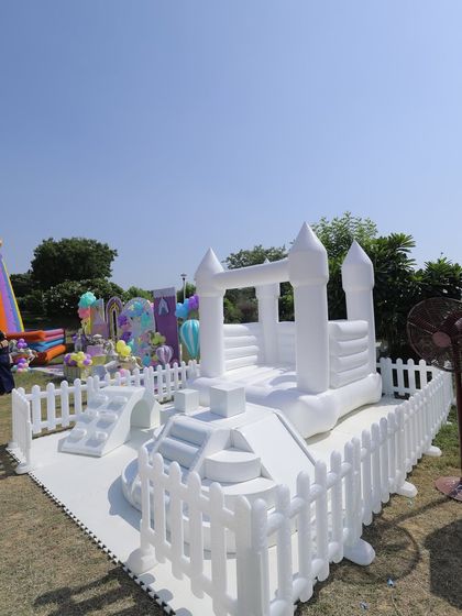 An all-white bouncy castle adds a touch of modern fun to this outdoor carnival party. Enclosed by a classic white picket fence, it provides a safe and aesthetically pleasing play area for the little guests.
