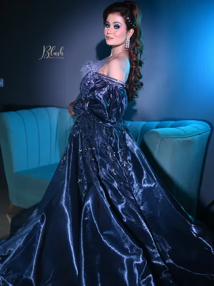 A dramatic, full-length shot of a cocktail gown look. The cool-toned blue lighting enhances the metallic sheen of the dress and the bold makeup.