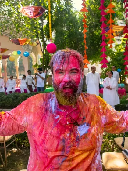 A portrait of a guest fully immersed in the Holi festivities, his face and clothes covered in a rainbow of colors.