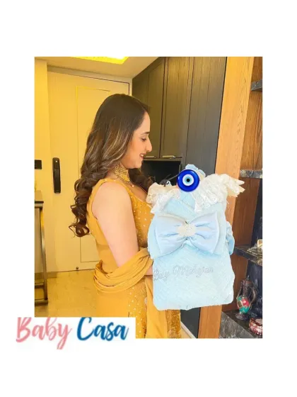 A proud auntie holds a special gift for her nephew. This personalized baby wrap in soft blue velvet is adorned with a large bow and an evil eye charm for protection and love.