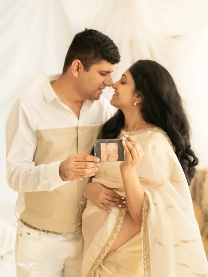 A tender moment between a couple, sharing their joy as they look at their baby's first sonogram. The mother-to-be is dressed in a beautiful cream saree, captured in a soft, light-filled boho setting, making for a warm and intimate pregnancy portrait.