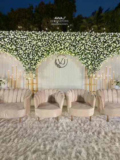 A close-up of the elegant seating on the all-white stage, with a custom monogram and a cascading canopy of white flowers creating a dreamy, romantic setting.