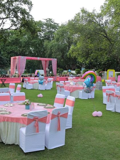A wide view of the guest seating area for the "Sunshine & Pastel Rainbows" party. The tables are decorated with pink and white linens, and the entire lawn is filled with themed elements.