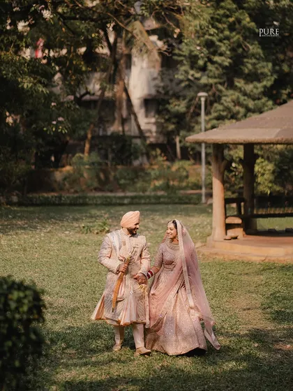 A beautiful wide shot of the couple in a park setting. The natural light and lush greenery provide a perfect backdrop for this romantic Sikh wedding portrait.