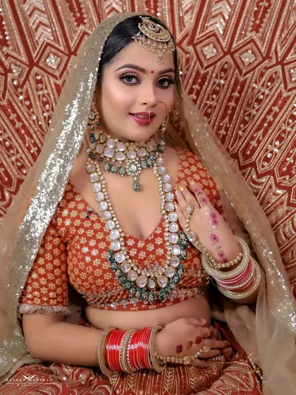 A bright, seated portrait against a richly patterned red backdrop, showcasing the full bridal look.