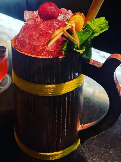 A vibrant red cocktail served in a rustic wooden mug. We have a wide variety of unique glassware to match any theme, from tiki parties to medieval banquets.