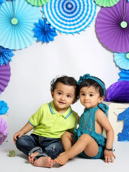 A beautiful portrait of one-year-old twins in a cool-toned color scheme of blues and purples. Their coordinated outfits look fantastic against the paper fan backdrop.