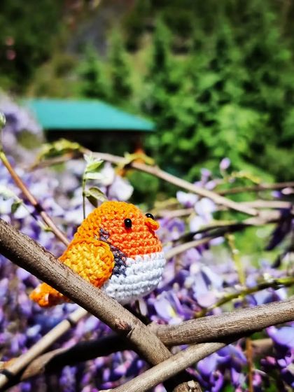 Titli the bird perched among beautiful purple flowers. The contrast of the orange yarn against the natural background is just lovely.