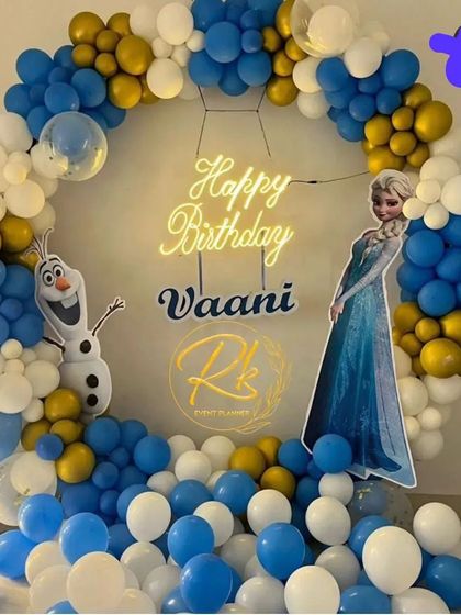 A magical Frozen-themed birthday party. This setup features a circular balloon arch in icy blue, white, and gold, with cutouts of Elsa and Olaf, all centered around a 'Happy Birthday' neon sign for a cool celebration.