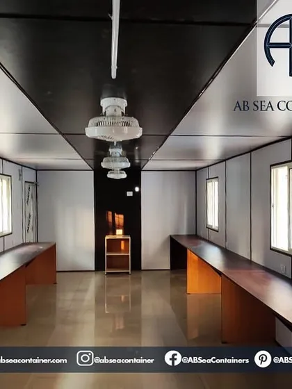 This image shows the clean and functional interior of a container office. It is equipped with long desks, lighting, and fans, creating a productive workspace for any remote site.
