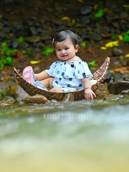 An adorable baby girl sitting in a crescent-moon-shaped boat in a stream, a magical outdoor portrait.