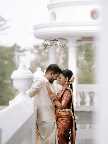 A quiet moment of togetherness captured against a classic white colonnade. We focus on capturing the gentle connection between two souls, preserving the authentic feeling of your wedding day in our South Indian wedding photography.