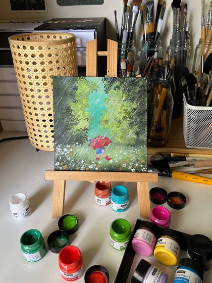 The rainy day painting displayed on a mini easel, with the colorful paint pots arranged around it.