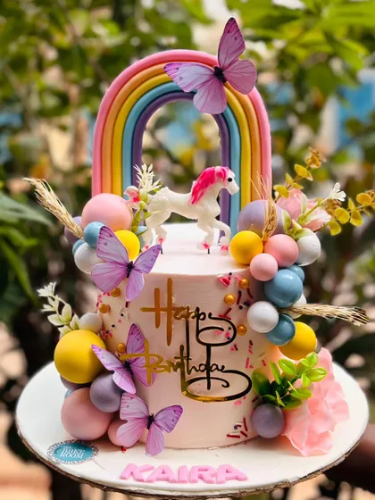 A dreamy unicorn and rainbow cake for Kaira's birthday. This design is adorned with pastel-colored spheres, delicate butterflies, and a beautiful rainbow, creating a truly magical centerpiece.