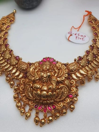 A stunning temple necklace with a Goddess Lakshmi seated on a lotus as the central pendant. The necklace is crafted from 92.5 silver with gold plating and adorned with pink stones.