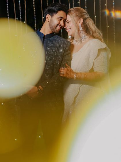 An artistic shot of a cross-cultural couple sharing an intimate moment during their Sangeet, with beautiful bokeh effects from the lights.
