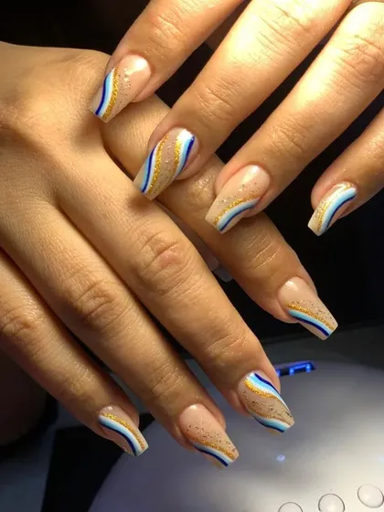 A beautiful design with a nude base and wavy stripes of blue, white, and gold glitter.