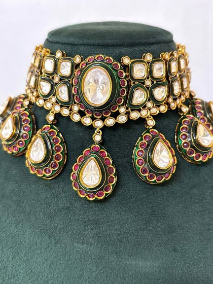 A close-up of a bridal choker with large Kundan stones and green and red Meenakari enamel work. This statement piece is available for rent for your special day.