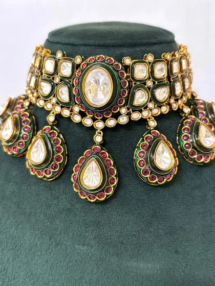 A close-up of a bridal choker with large Kundan stones and green and red Meenakari enamel work. This statement piece is available for rent for your special day.