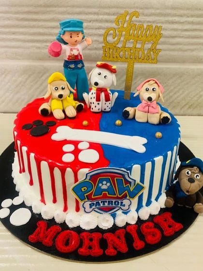 A vibrant red and blue Paw Patrol cake with drip effects. This design includes fondant bones, paw prints, and several members of the patrol team.