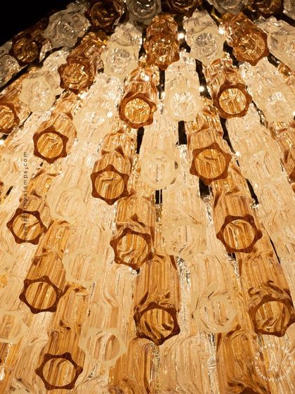 A colossal chandelier featuring tiers of fluted glass in warm amber and clear tones. Its grand scale and textured glass elements make it a stunning centerpiece, ideal for large, open spaces that require a significant and artistic lighting installation.