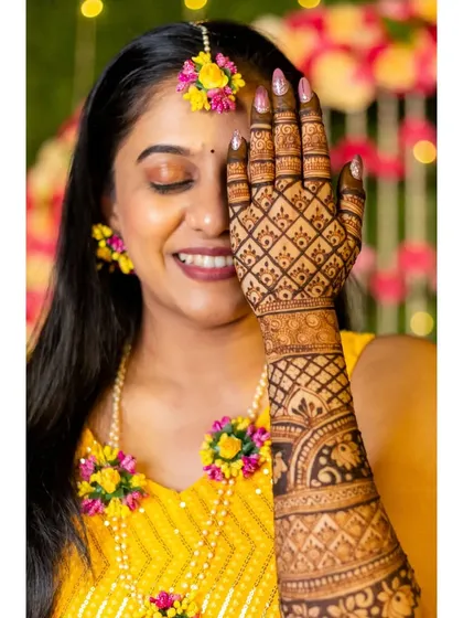 A lovely portrait of the bride, her face partially covered by her hand, drawing attention to the beautiful mehendi and her happy smile.