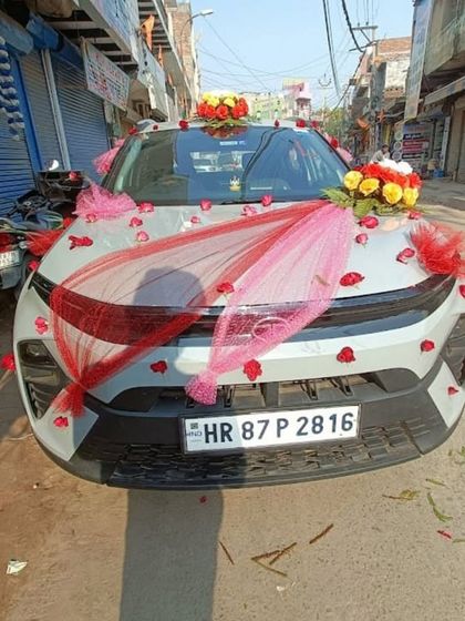 This car decoration uses red and pink netting draped across the bonnet, accented with flower bouquets and scattered rose petals for a simple and affordable option.